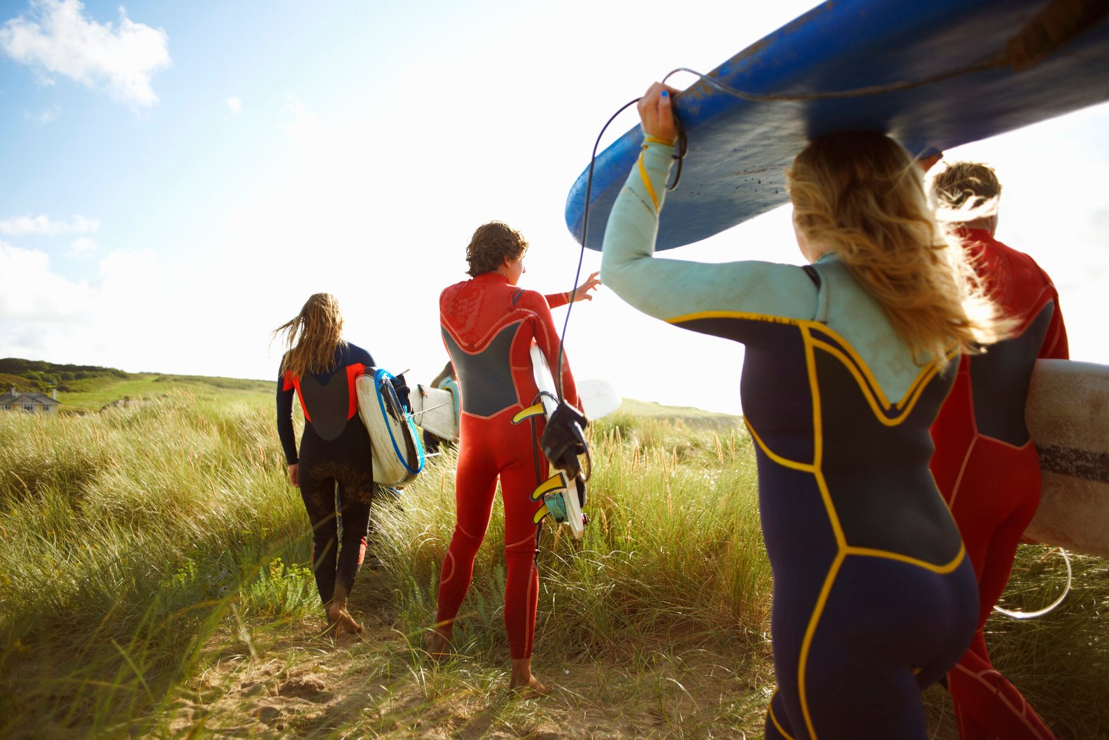 Group of surfers heading towards beach, carrying surfboards, rear view