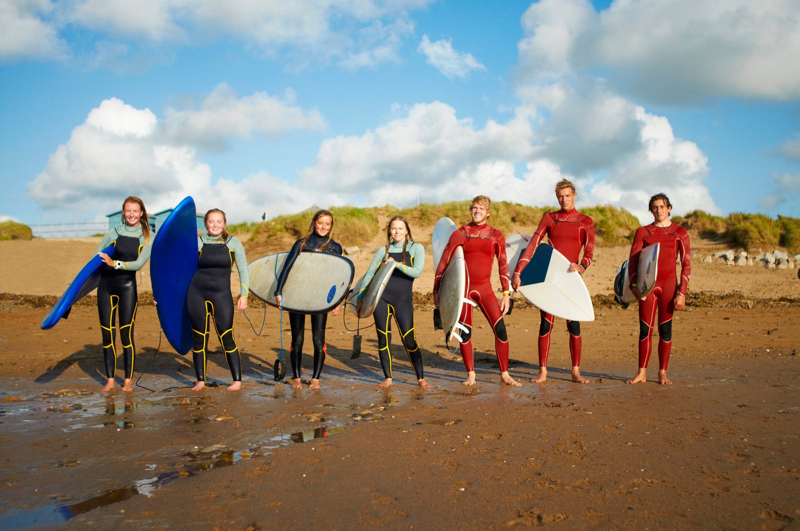 Group of surfers, standing on beach, holding surfboards