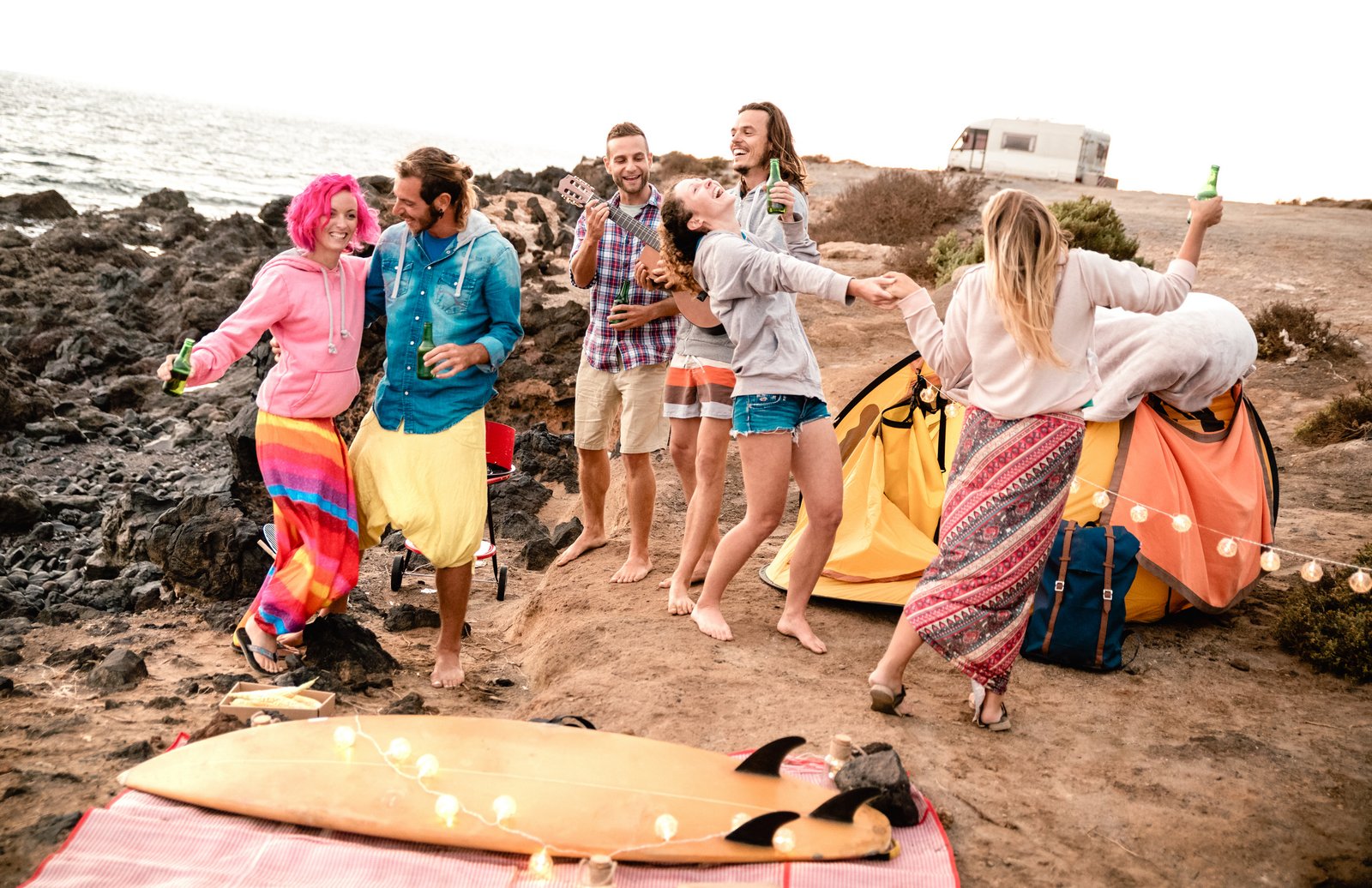 Hipster friends having fun together at beach party on camping time - Wanderlust and alternative travel concept with young people dancing and drinking beer at summer surf camp - Warm vintage filter